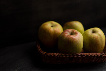 Some yellow with red apples in a basket on a black wooden table  
