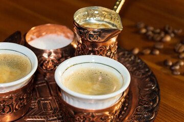 Traditional, oriental coffee cooked in turkish copper coffee pot poured in a cup. Oriental plate, pot and coffee cup. Coffe beans on table.