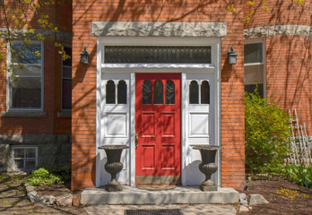 Exterior daytime view of entrance to red brick building showing red entrance door with leaded glass inserts, sidelights and transom window, lamps and planters, nobody - obrazy, fototapety, plakaty