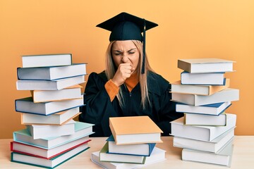 Young caucasian woman wearing graduation ceremony robe sitting on the table feeling unwell and coughing as symptom for cold or bronchitis. health care concept.