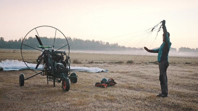 Glider checking parachute cords, stretching them and looking for tangling. Tandem motor powered paragliding at twilight. 