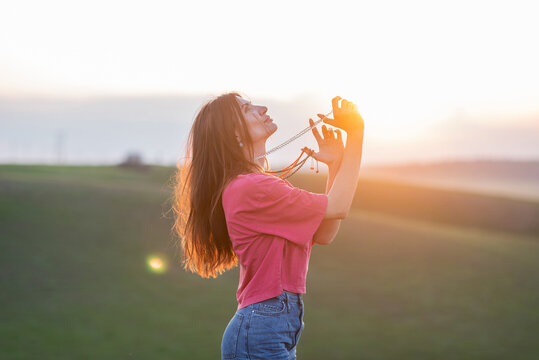 A beautiful young girl in bright clothes stands in the steppe and looks at the sky, beads hang around her neck, her hair is illuminated by the setting sun. Buddhism