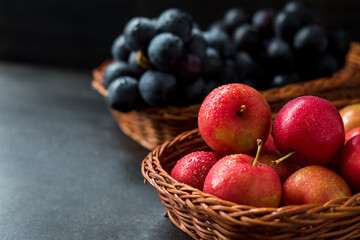 Red and fresh plums with grapes in a basket on a black table 