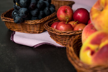 Some plums, peaches and grapes in some baskets on a black table with a black background