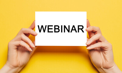 Female hands hold card paper with text webinar on a yellow background. Education and study concept