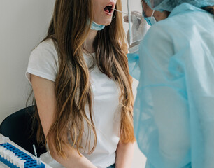 Fototapeta premium Doctor in protective workwear taking nose swab test from young woman. Close-up of woman having PCR or PLR testing at the hospital. Woman being screened for coronavirus in a laboratory.