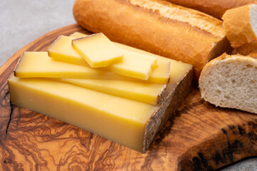 French food -  piece of cheese comte made from cow milk in region Franche-Comte in France and fresh baked baguette bread.
