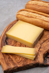 French food -  piece of cheese comte made from cow milk in region Franche-Comte in France and fresh baked baguette bread.