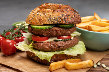 Tasty vegetarian vegan lunch with double decker hamburger made from plant based soya beans burger, organic bun with seeds and fresh vegetables and french fried potatoes