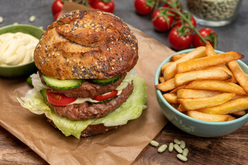 Tasty vegetarian vegan lunch with double decker hamburger made from plant based soya beans burger, organic bun with seeds and fresh vegetables and french fried potatoes