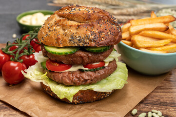 Tasty vegetarian vegan lunch with double decker hamburger made from plant based soya beans burger, organic bun with seeds and fresh vegetables and french fried potatoes