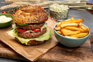 Tasty vegetarian vegan lunch with double decker hamburger made from plant based soya beans burger, organic bun with seeds and fresh vegetables and french fried potatoes