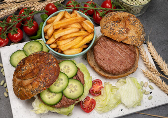 Tasty vegetarian vegan lunch with hamburger made from plant based soya beans burger, organic bun with seeds and fresh vegetables and french fried potatoes