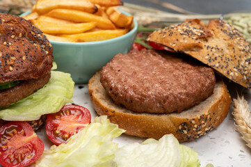 Tasty vegetarian vegan lunch with hamburger made from plant based soya beans burger, organic bun with seeds and fresh vegetables and french fried potatoes