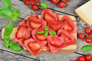 Red heart ravioli with tomato, mozzarella and basil on a wood background