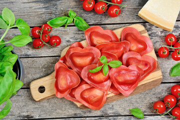 Red heart ravioli with tomato, mozzarella and basil on a wood background