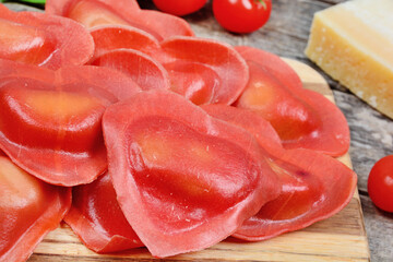 Red heart ravioli with cherry tomato, mozzarella, parmesan and basil on cutting board