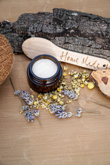 Obraz na płótnie Canvas Homemade natural face cream or body cream in amber glass jar with herbs of chamomile flowers and lavender flowers on the beige, wooden background. 