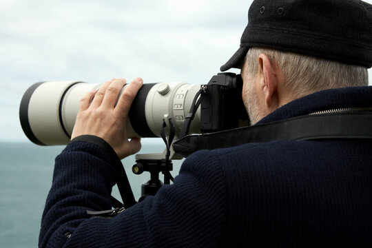  Landscape photography. A cut-off image of an adult male taking photos with a camera with a telephoto lens. The lens is supported by a monopod.