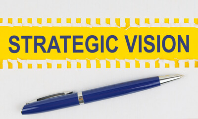 On the table are two sheets from a notebook and a pen on a yellow background written - STRATEGIC VISION