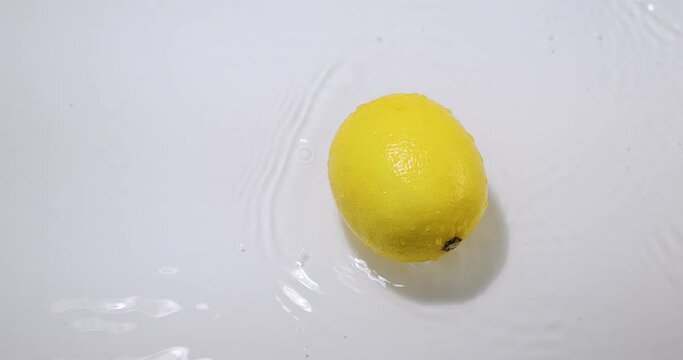 Fresh yellow lemons rolling in water with splashing, natural fruits citrons on white studio backdrop, top view