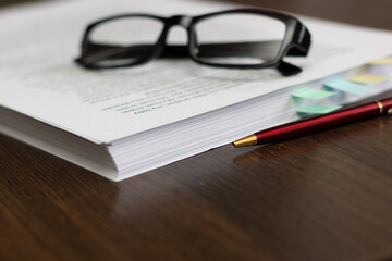 Paper folder with documents on the table, glasses, pen.