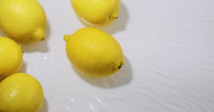 Lemons lying in flowing water, natural fruits citron on white studio backdrop, vitamins and healthy eating concept