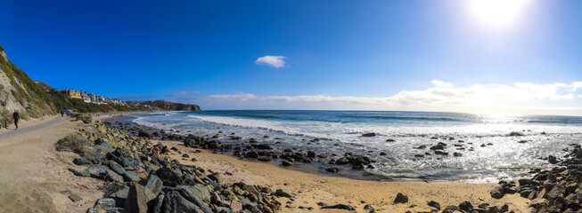 a stunning panoramic shot of the vast blue ocean water with waves rolling in and people walking along the beach on silky brown sand with blue sky and clouds at Dana Strands Beach in Dana Point CA - obrazy, fototapety, plakaty