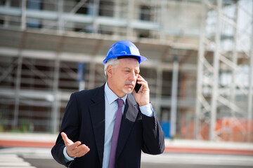 Angry architect talking on the cellphone in front of construction site