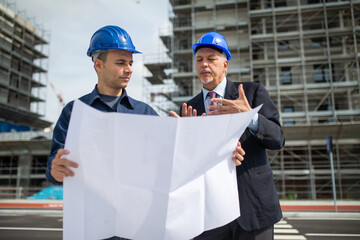 Architect talking to the site manager in front of a construction site building