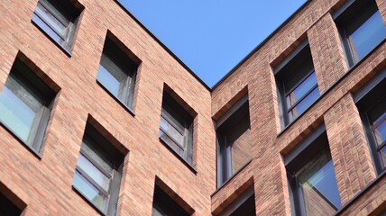 Fototapeta premium Modern brick and glass facade of the office building. A contrasting combination of sky and brick texture on a building. Architectural facade of a red brick building..