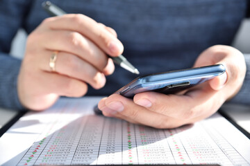 Trader man with pen in hand using smart phone with stock statistic