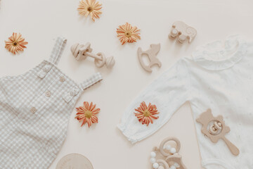 Clothes for baby and newborns: white bodysuits and accessories neutral beige and brown colors. Eco friendly wooden toys on Light background, top view, flat lay.