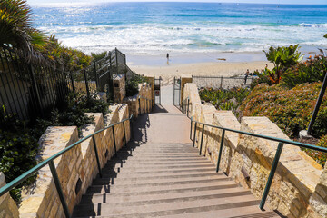 a white stone staircase to the beach with silky sand and blue ocean water surrounded by lush green...