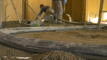 CLOSE UP: Rubber hose pulsates as contractors pour concrete across the ground.