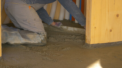 CLOSE UP: Kneeling contractor levels the wet concrete covering the ground.