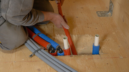 CLOSE UP: Unrecognizable plumber pushes hoses down a hole in the hardwood floor.