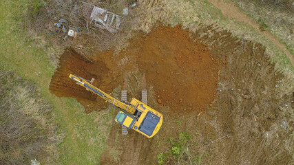 TOP DOWN: Drone point of view of yellow excavator digging a hole in countryside