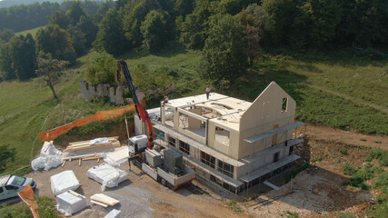AERIAL: Truck boom lifts a massive CLT wall panel as workers assemble a house.