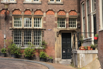 Fototapeta na wymiar Amsterdam Picturesque Street View with Old Building Facade, Entrance Steps and Green Plants in Pots on the Pavement in the Red Light District