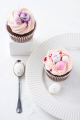 Two Easter chocolate cupcakes with caramel filling and decoration of small Easter eggs from marzipan on a white porcelain plate. Selective focus