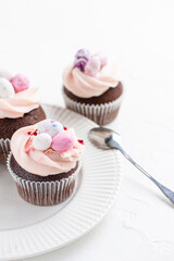 Three Easter chocolate cupcakes with caramel filling and decoration of small Easter eggs from marzipan on a white porcelain plate. Selective focus