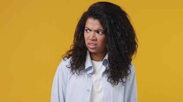 Young african woman curly hair 20s years old wear blue white t shirt look aside around one guy nice other disapprovingly different emotions like dislike isolated on yellow color wall background studio
