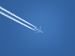 An airplane flying hish across the sky with vaportrails diagonaly dehind it.
