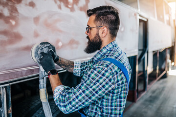 Professional car body worker fixing and repairing bus at maintenance service or garage. He is...