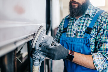 Professional car body worker fixing and repairing bus at maintenance service or garage. He is...