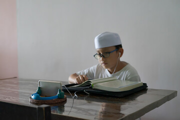 Asian kid reading Al-Quran through video call during education and learning from home for kid. Homeschooling during quarantine using smartphone.