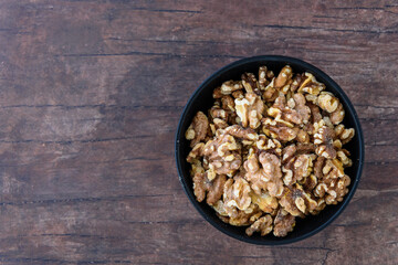 Toasted walnuts in a round black ceramic bowl on a wooden background
