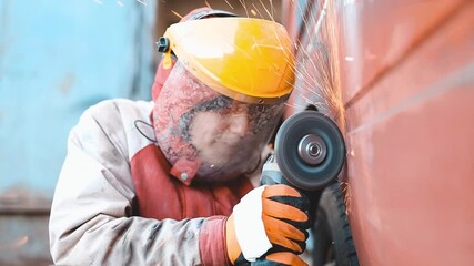 man car mechanic in a protective helmet grinds welded seams with a grinder, body repair