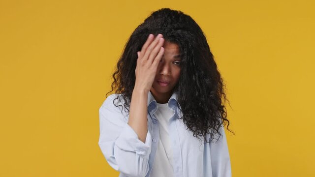 Sad upset ashamed tired young african woman curly hair 20s years old wears blue white t shirt put hand on face facepalm epic fail mistaken omg gesture isolated on yellow color wall background studio